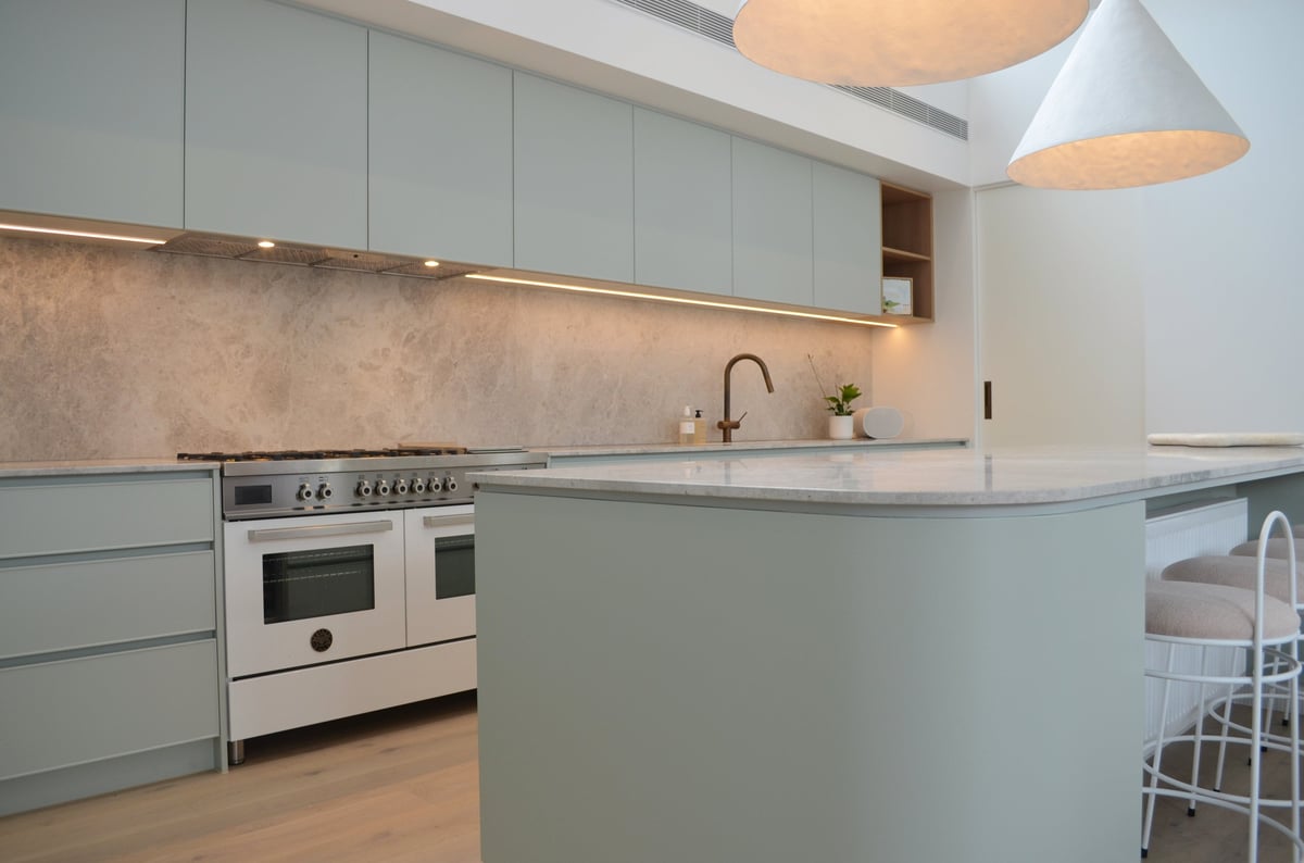 Modern kitchen with sage green cabinetry, white range oven, waterfall island countertop, and pendant lighting