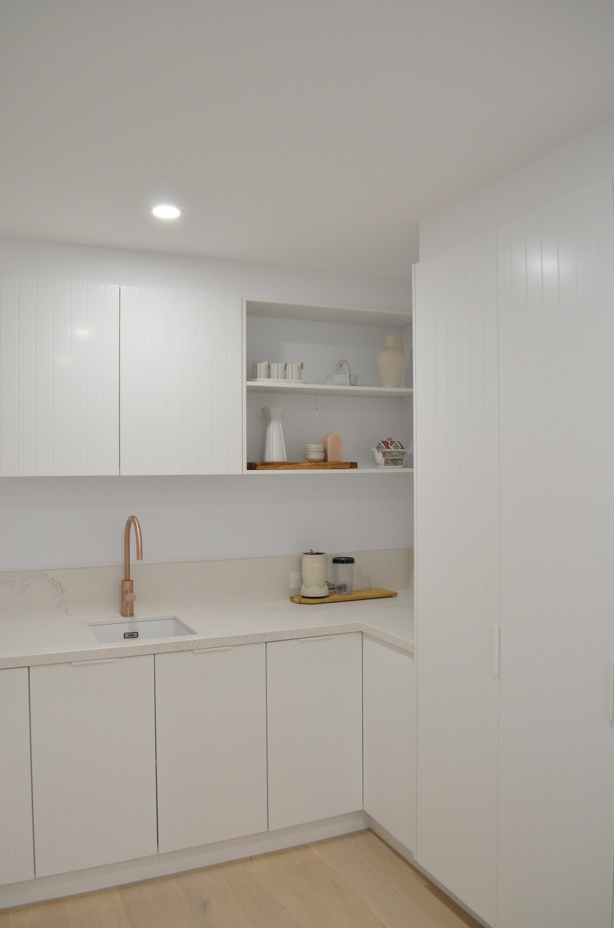 Modern minimalist bathroom with white cabinetry, floating shelves, small sink, and wooden floor