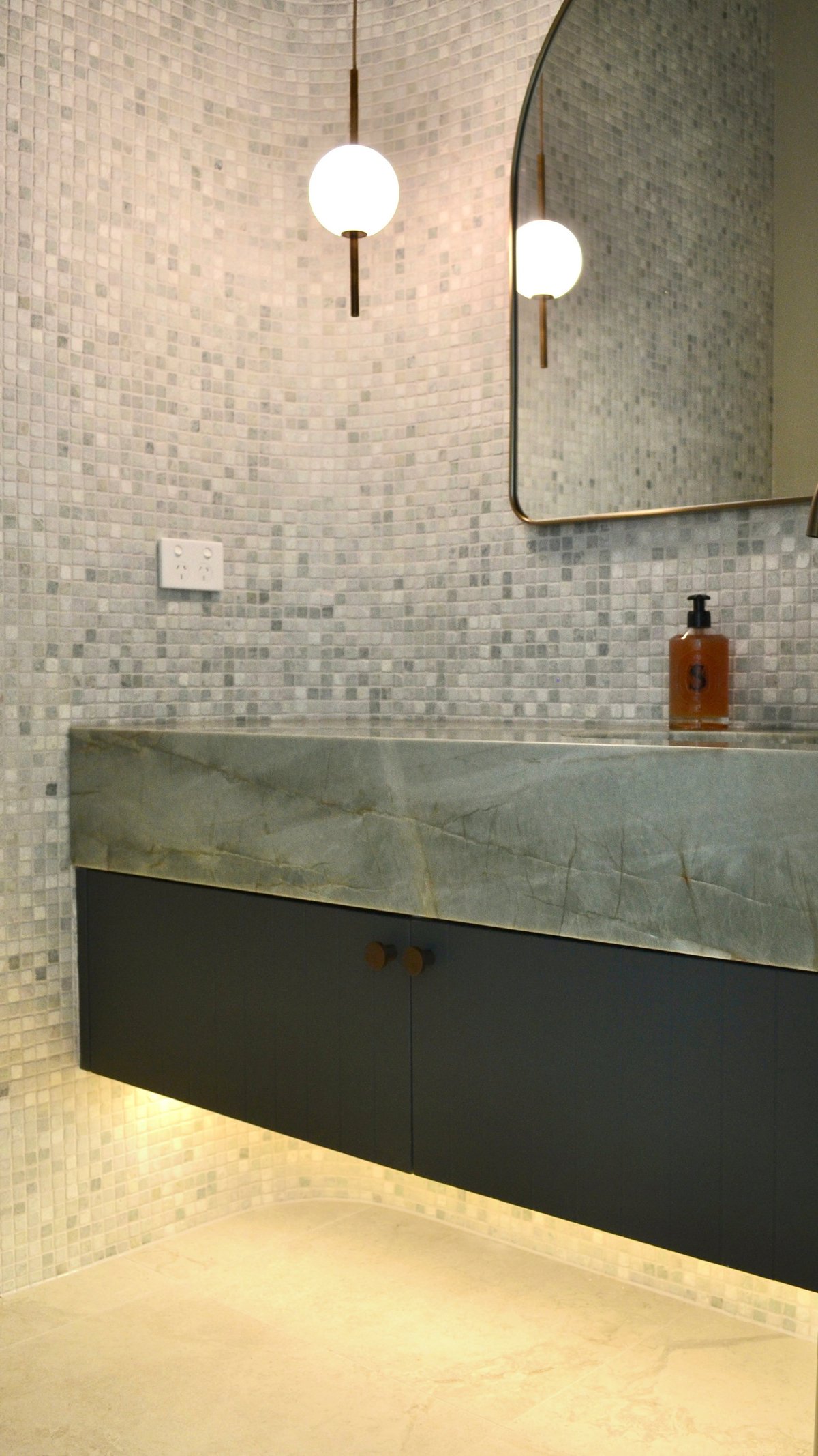 Modern bathroom with white mosaic tile walls, floating black vanity with concrete sink, round mirror, and two pendant lights