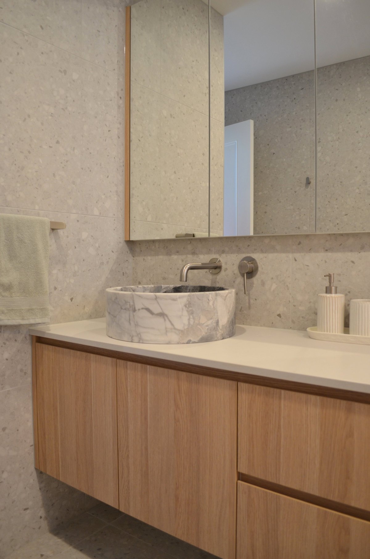 Modern bathroom with marble stone sink, wood vanity cabinet, mirrored medicine cabinet, and neutral tile walls