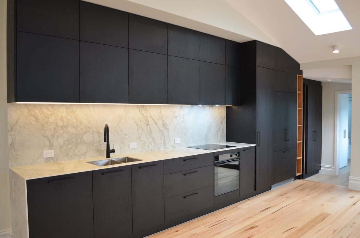 Modern kitchen with black cabinetry, marble backsplash, white countertop, and wooden flooring