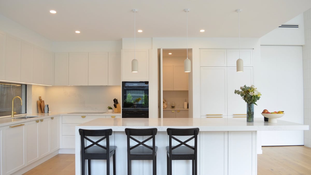 Modern white kitchen with island, black bar stools, built-in appliances, and pendant lighting