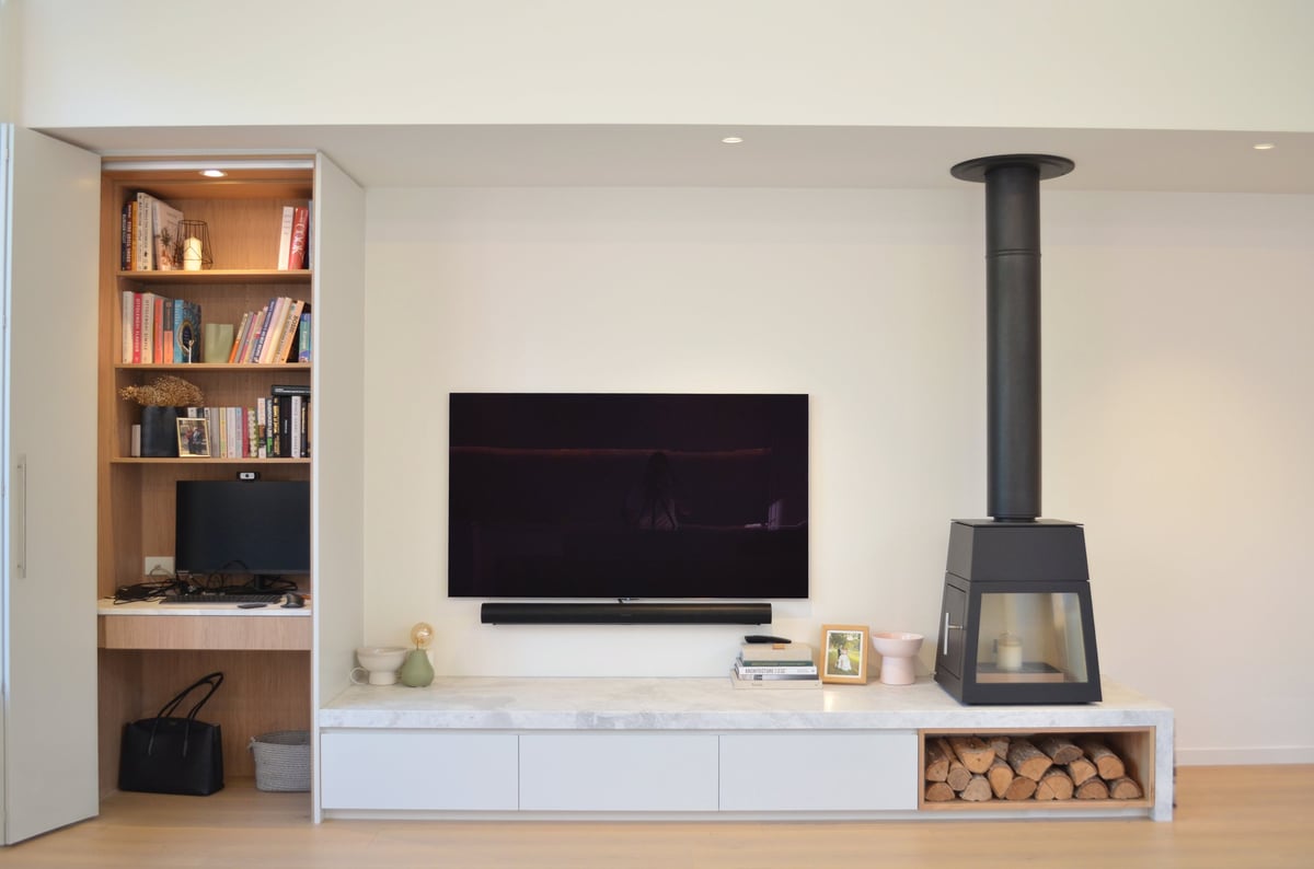 Modern living room with wall-mounted TV, white media console, wooden bookshelf, and black wood stove