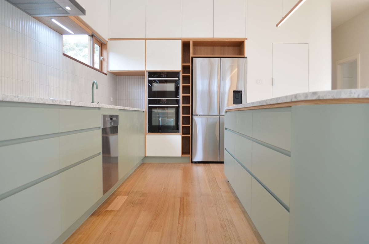 Modern galley kitchen with light green cabinets, stainless steel appliances, and natural wood flooring
