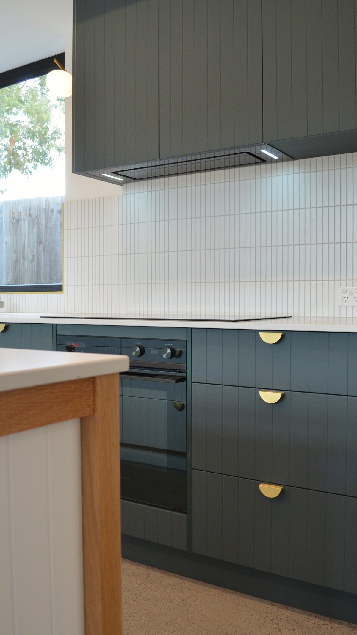 Modern kitchen with dark green cabinetry, white subway tile backsplash, black range hood, and brass hardware accents